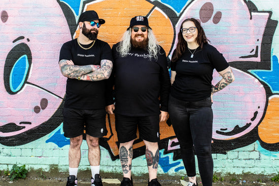 Burgo, Jase, and Dana standing in front of a graffiti wall wearing Happy Pessimist tees.